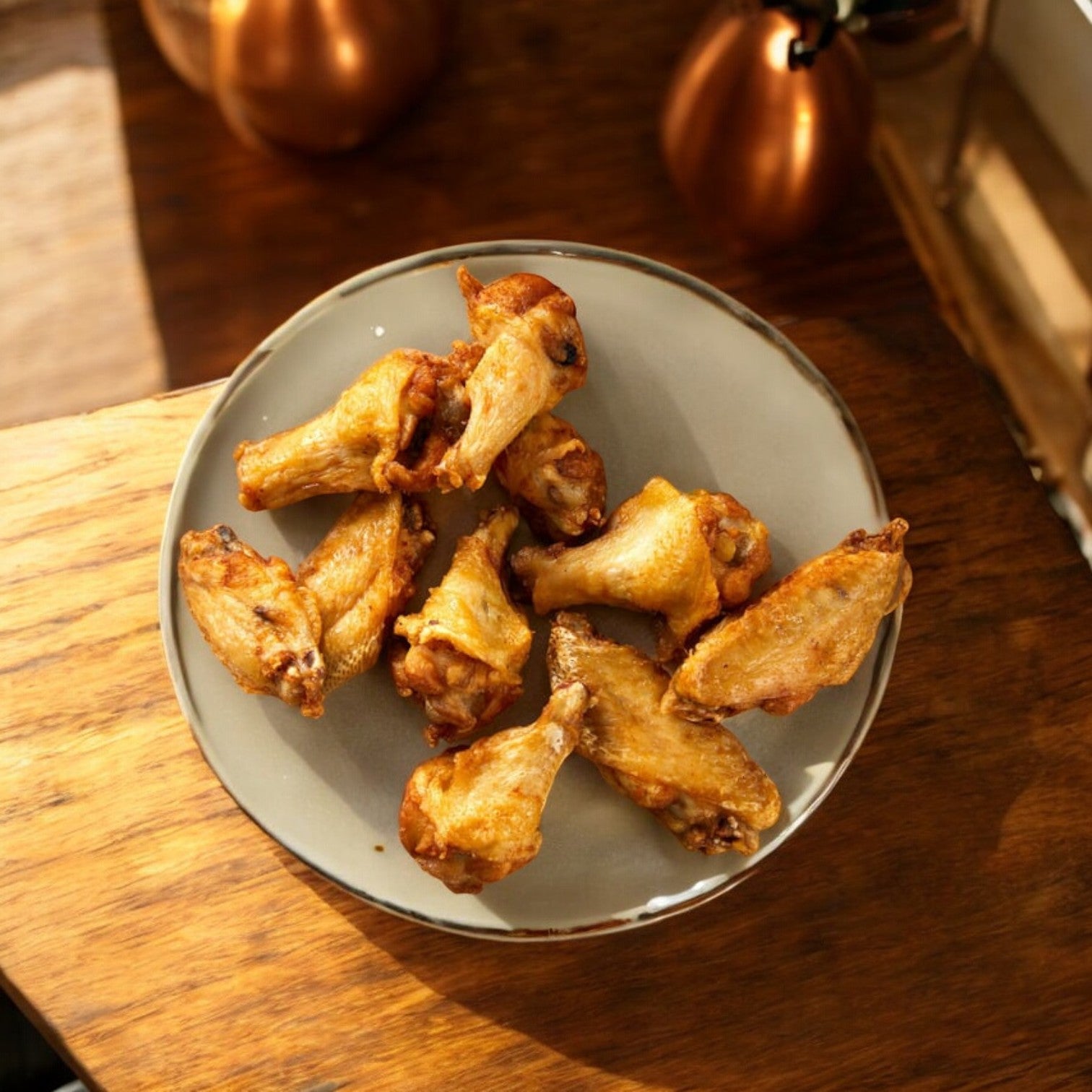A gray plate holds cooked Easy Lunches Chicken Wings, Kirkland Signature-10 lbs.-3 Bags-30 Pounds Total, on a wooden table in warm lighting, ideal for party servings.