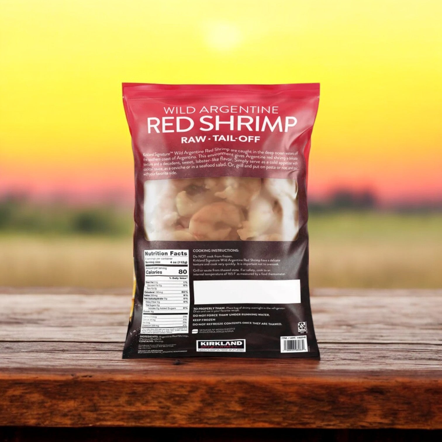 A bag of Easy Lunches Kirkland Signature Wild Argentine Raw Shrimp (20/40, 2 lbs per bag, 3 bags, 6 lbs total) rests on a wooden surface outdoors with a sunset and grassy background, highlighting premium wild-caught shrimp.