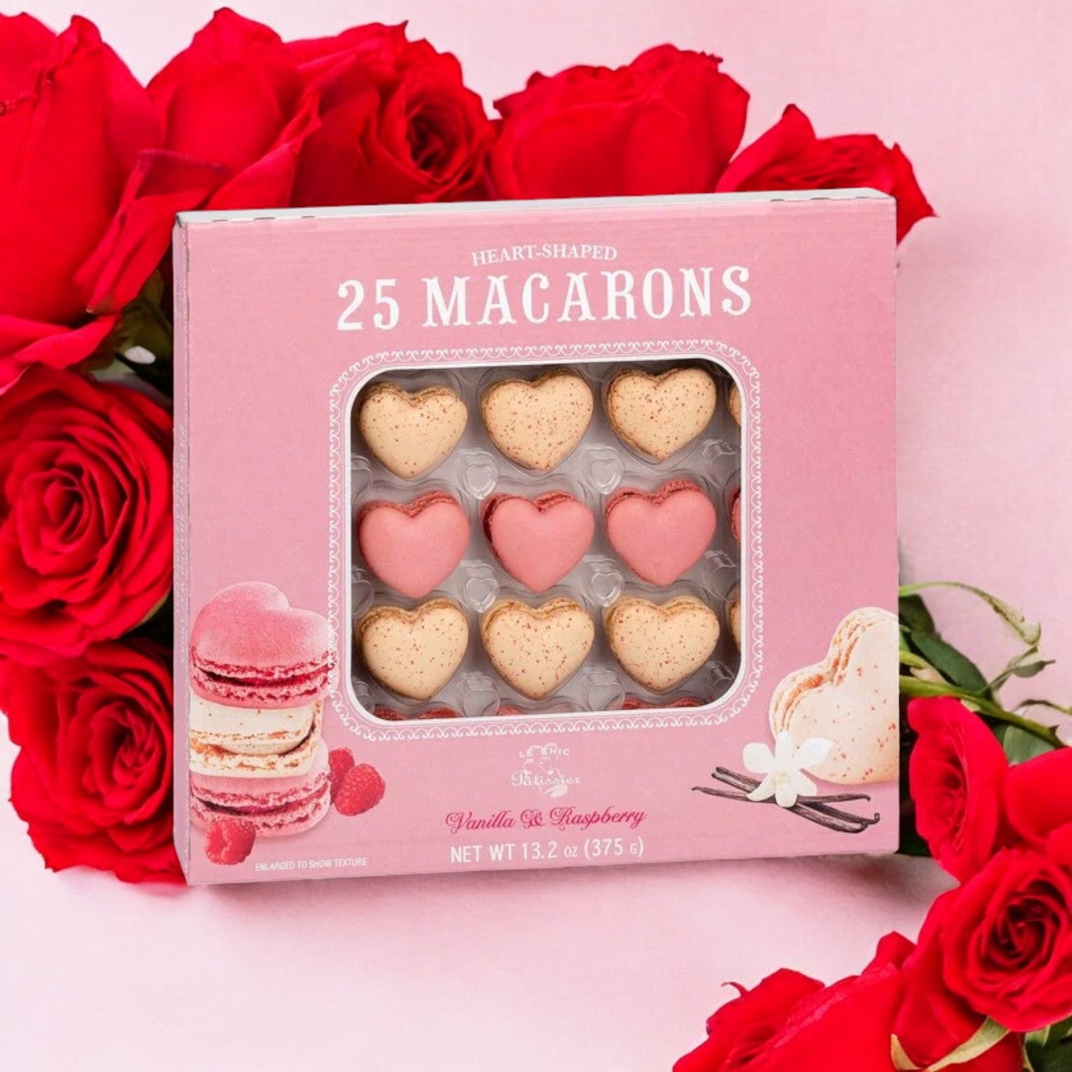 A 25-count box of Le Chic Patissier Heart Macaron in vanilla and raspberry flavors, set against a pink background with red roses.