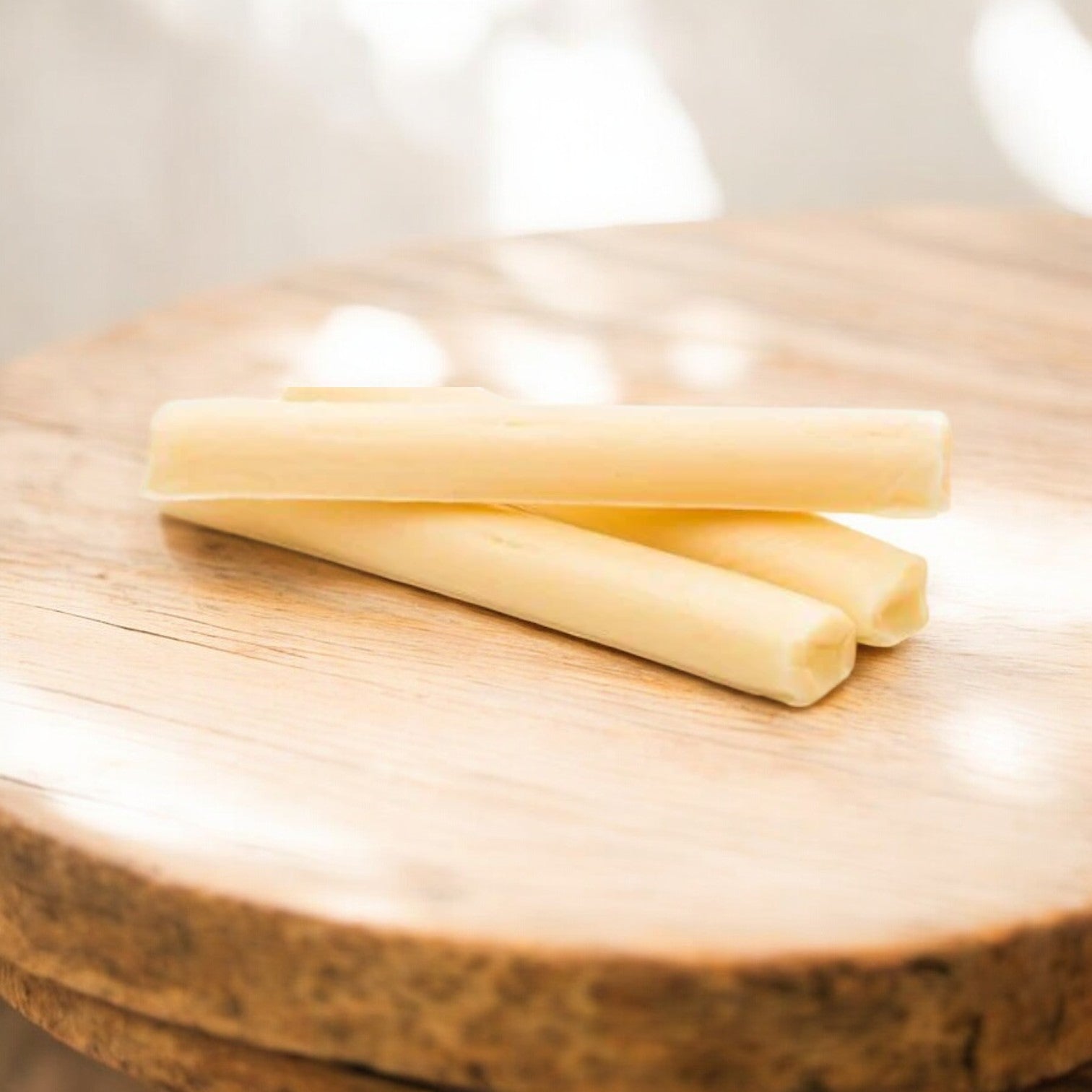 Three pieces of Arrezzio Imperial Cheese Mozzarella String, 1 oz. - 168 Case Count, are placed on a wooden surface, with soft light creating a gentle shadow—a high-protein snack in convenient packaging from Arrezzio Imperial.