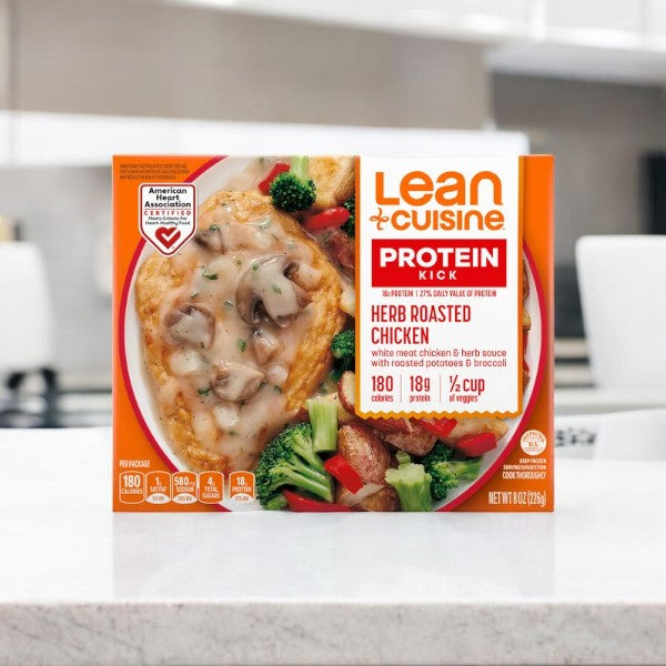 A Lean Cuisine Herb Roasted Chicken meal featuring a chicken breast with herb sauce, roasted potatoes, and broccoli sits on a kitchen countertop.