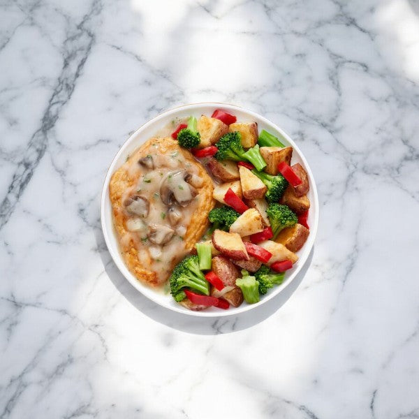 A plate featuring Lean Cuisine's Herb Roasted Chicken, paired with roasted potatoes and steamed red bell peppers on a marble surface, all topped with a rich, creamy Alfredo sauce.