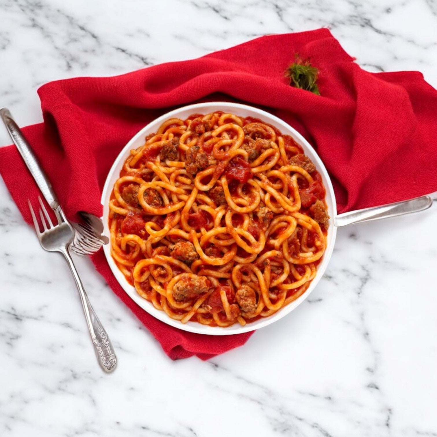 A bowl of Lean Cuisine Spaghetti with Meat Sauce with Mushrooms and Basil is placed on a red cloth, with a fork and spoon beside it, offering a quick and convenient meal perfect for busy days.