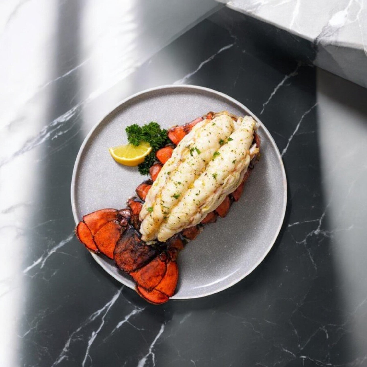 Sysco's North Atlantic premium lobster tail, plated on gray stoneware with fresh herbs, parsley, and a lemon wedge, elegantly displayed on a sleek marble surface.