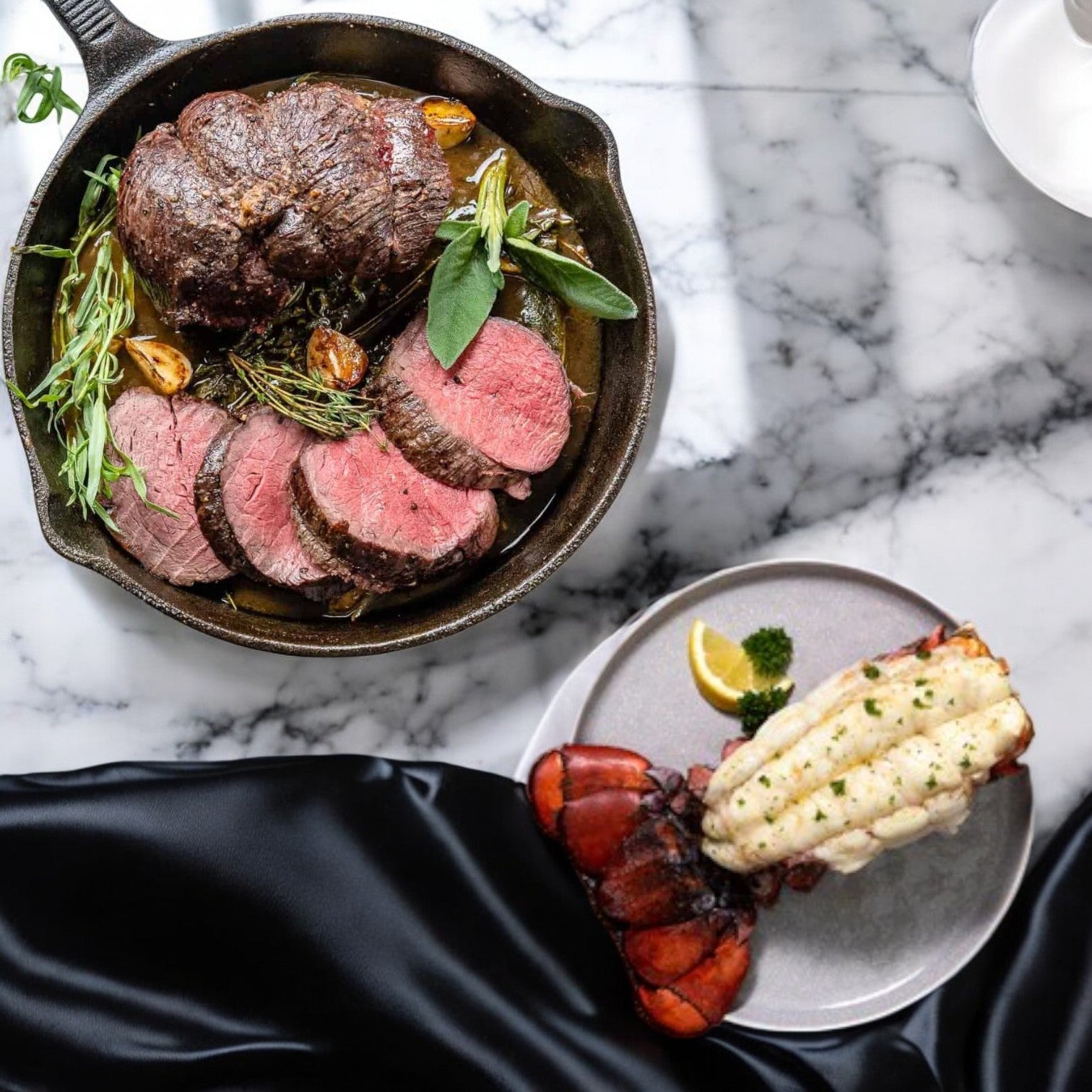 The Easy Lunches Surf and Turf! featuring USDA Choice Beef Loin Tenderloin Steak - Filet Mignon and 5 pounds of frozen Netuno Lobster Tails creates a classic appeal, elegantly presented on a marble table partially draped in black fabric. Enjoy free shipping with your order!