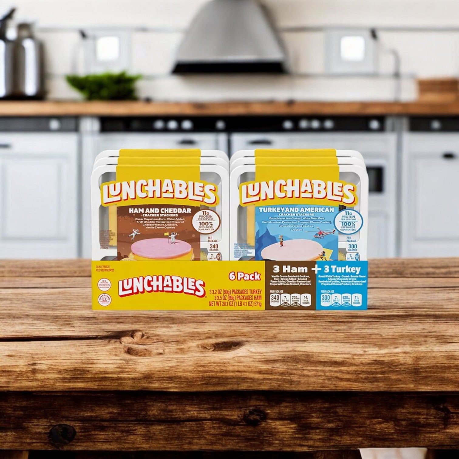 Displayed on a kitchen counter are two packs from the Lunchables Cracker Stackers Snack Kit Variety Pack, 6 pk. One features Ham and Cheddar, while the other contains Turkey and American. The blurred background reveals a modern kitchen with white cabinets, providing an ideal setting to showcase these convenient snacks for on-the-go munching.