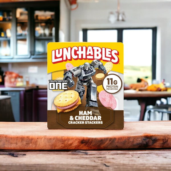 A pack of Lunchables Ham & Cheddar Cheese, 3.5 oz., branded with a Transformers character, is displayed on a wooden counter in a kitchen setting. This convenient meal is perfect for on-the-go meals.