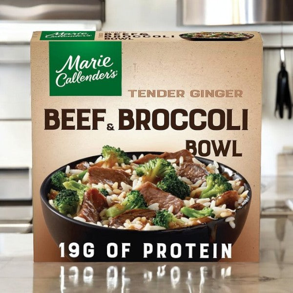 A box from the Marie Callender's Meals Bundle- featuring Tender Ginger Beef & Broccoli Bowl sits on a kitchen counter, showcasing a delightful dish of beef, broccoli, and rice. The packaging prominently features "19g of protein" in bold letters. Beside it, another meal from the bundle - the mouthwatering Aged Cheddar Cheesy Chicken & Rice Bowl - catches your eye for your next meal.