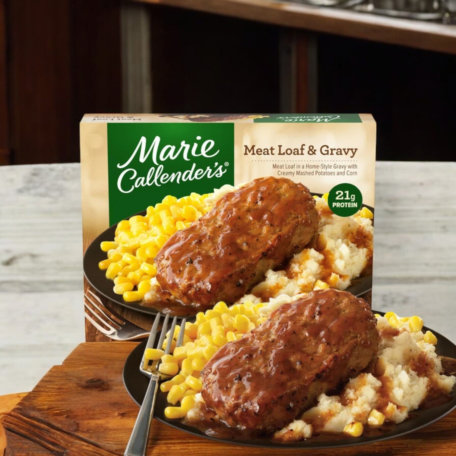 A Marie Callender's Meat Loaf & Gravy, 12.4 oz. - 1 Count meal with creamy mashed potatoes and corn is displayed on a wooden table next to its packaging. Reminiscent of the comfort in Marie Callender's Fettuccini with Alfredo sauce, the meal is plated and appears ready to eat.