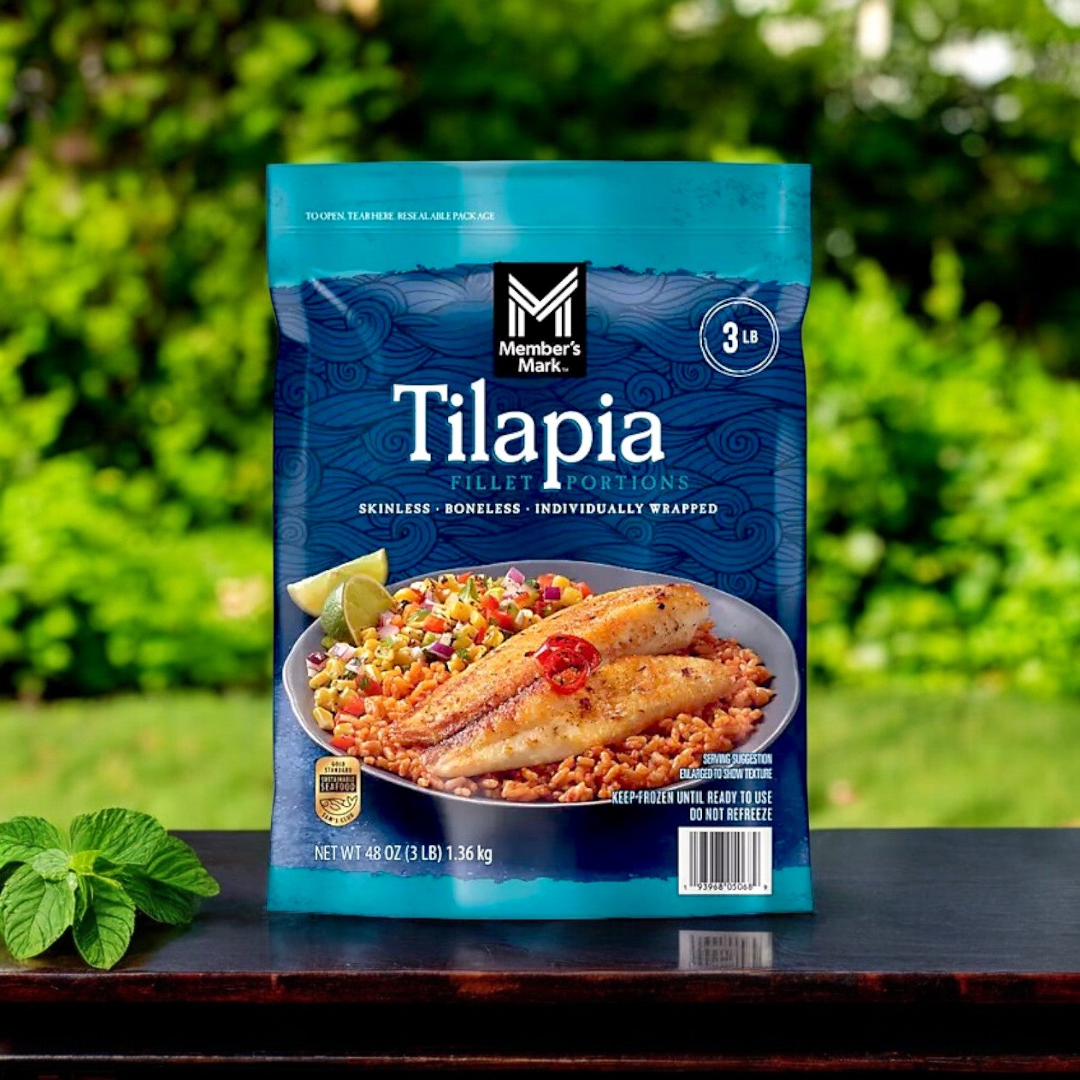 Displayed on a table with herbs, Member's Mark Farm-Raised Tilapia Fillet Portions are served alongside cooked fillets on a plate of rice. This 9-pound package offers skinless, boneless pieces individually wrapped, ensuring easy access to lean protein.