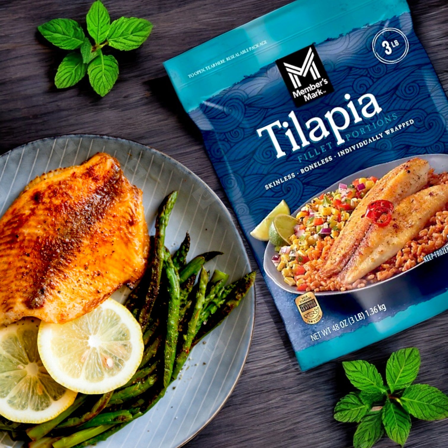 A Member's Mark Farm-Raised Tilapia Fillet Portion takes center stage, paired with lemon and asparagus. Nearby, the 3-pound bag of skinless, boneless frozen Tilapia rests on a dark wooden surface with mint leaves, promising a protein-rich delight.