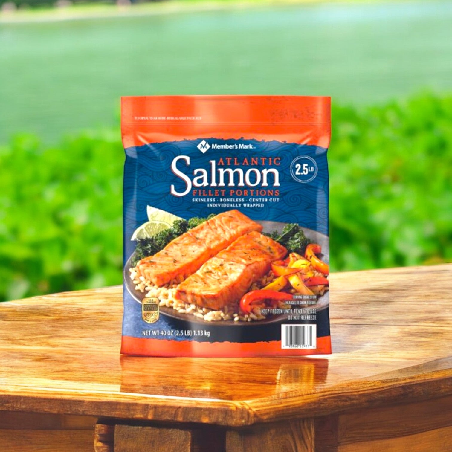 A 40 oz. bag of Member's Mark Atlantic Salmon Fillet Portions, known for being rich in Omega-3 Fatty Acids, sits on a wooden table outdoors with a blurred background of greenery and water.