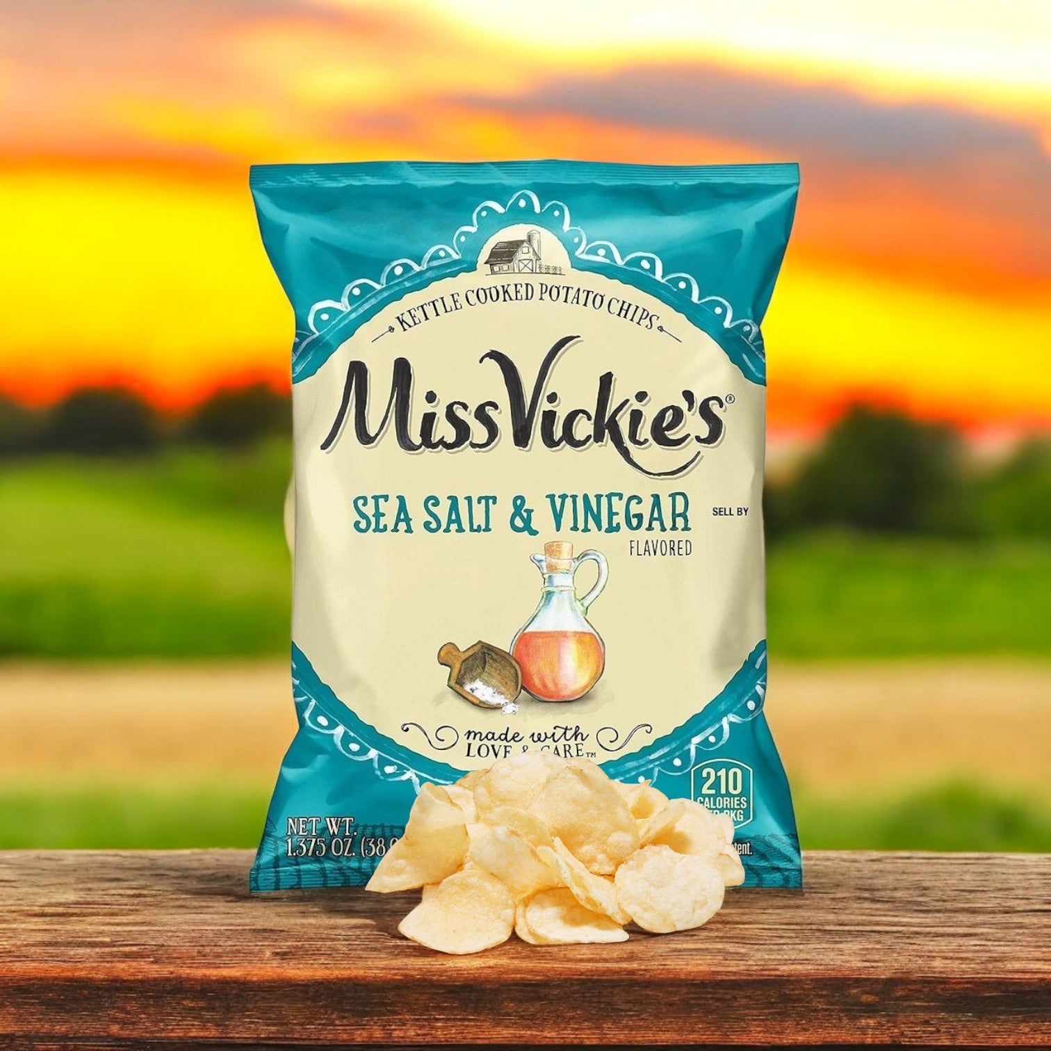 A bag of Miss Vickie's Potato Chips Salted & Vinegar Kettle 64/1.375 oz. rests on a wooden surface with a few crispy chips in front, set against a blurred sunset background, highlighting the bold flavors in every bite.