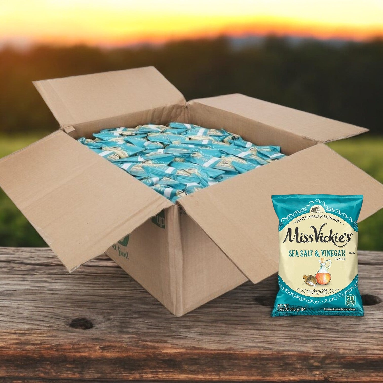 An open box on a wooden table reveals small bags of Miss Vickie's Potato Chips Salted & Vinegar Kettle 64/1.375 oz., each offering a crispy snack experience. One bag sits outside the box, tempting chip lovers with its bold flavor.