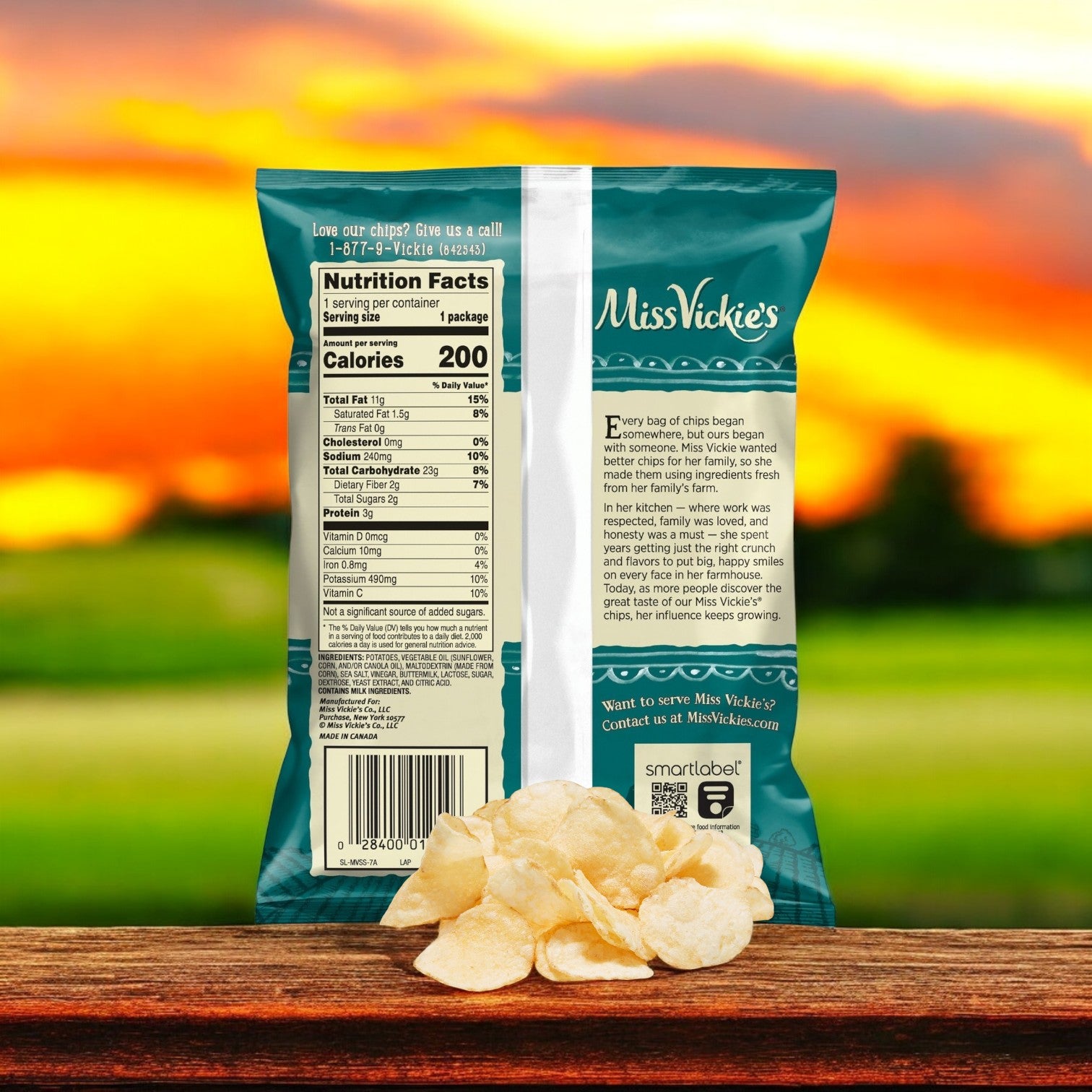 The back of a Miss Vickie's Potato Chips Salted & Vinegar Kettle bag is shown with nutrition facts, standing on a wooden surface against a blurred sunset background, inviting you to savor this bold and crispy snack.