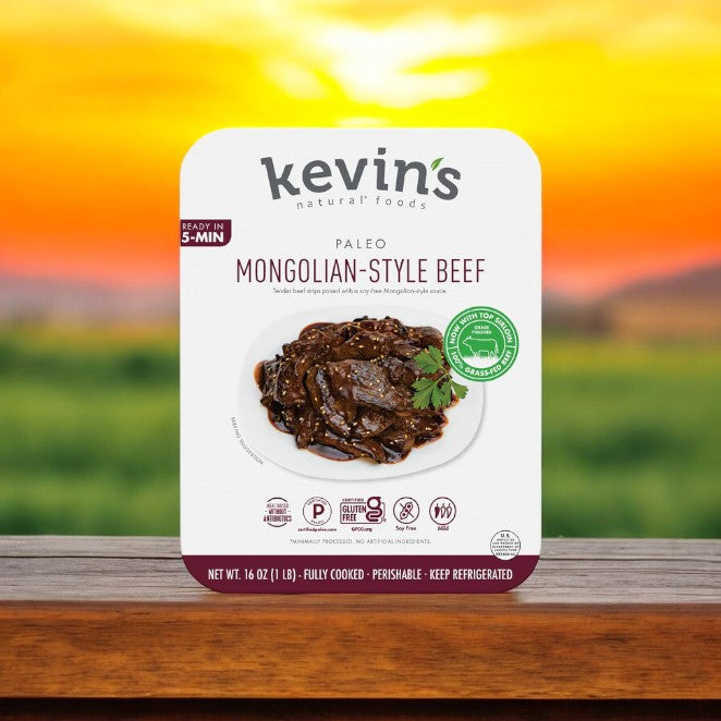 A package of Kevin's Mongolian Beef - 16 oz. - 1 Count rests on a wooden surface with a blurred outdoor sunset in the background, showcasing restaurant-quality cuisine made from all-natural ingredients by Kevin's.