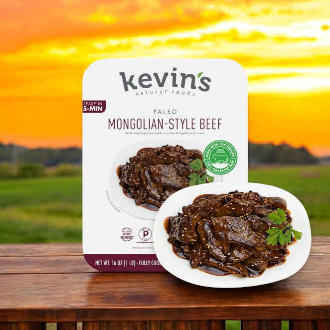 Kevin's Mongolian Beef - 16 oz. - 1 Count from Kevin's sits elegantly on a wooden table, accompanied by a plate of restaurant-quality cuisine. A sunset over a grassy field serves as an ideal backdrop, highlighting the all-natural ingredients.