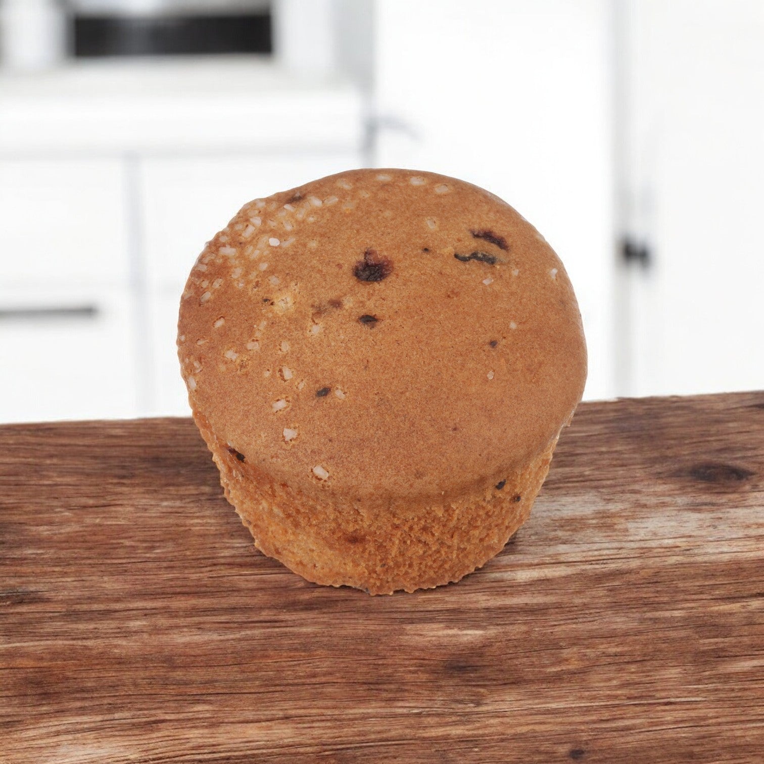 A Udi's Gluten-Free Blueberry Muffin, featuring small dark spots, rests on a wooden surface, exuding a classic and delicious appeal against the blurred background. This individually-wrapped muffin from Udi's comes in a 3 oz. size within a case of 36.