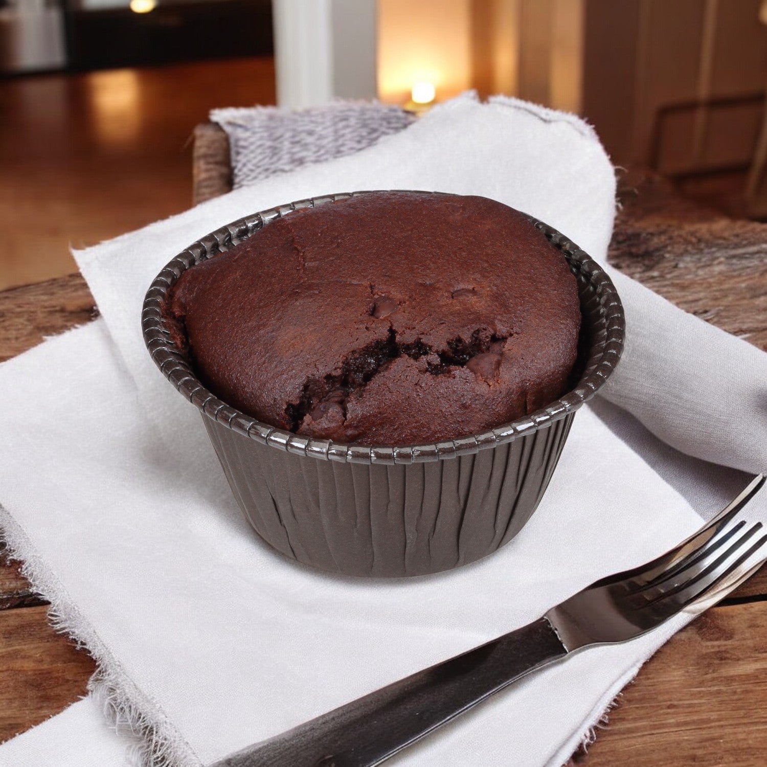 Udi's Double Chocolate Gluten-Free Muffin, individually wrapped in a cup on a napkin with a fork beside it on a wooden surface.