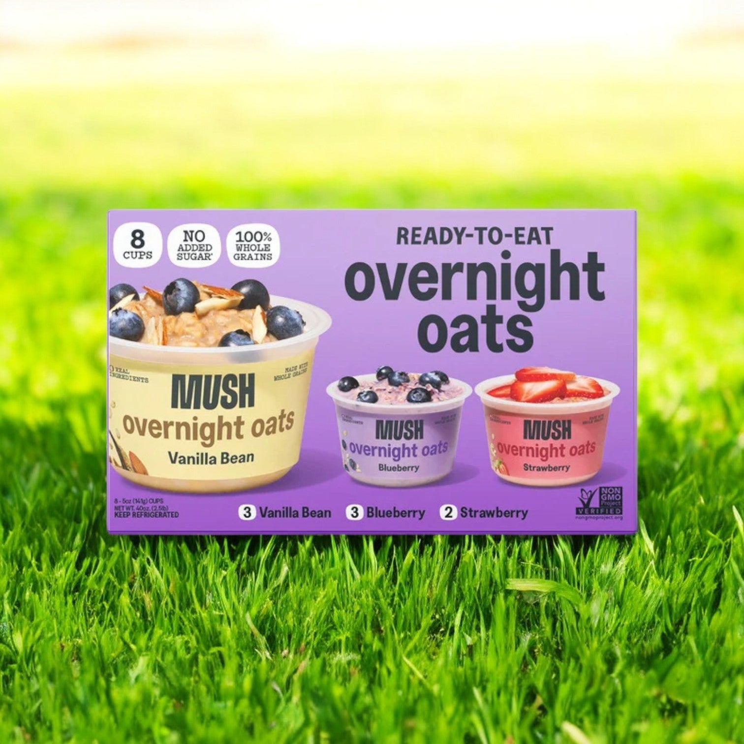 A pack of "Mush Overnight Oats Variety, 5 fl oz, 8 Count" from the brand Mush is displayed on the grass. This plant-based breakfast option offers delightful flavors of vanilla bean, blueberry, and strawberry. Each cup is made with 100% whole grains and contains no added sugar, making it an ideal choice for a wholesome start to your day.