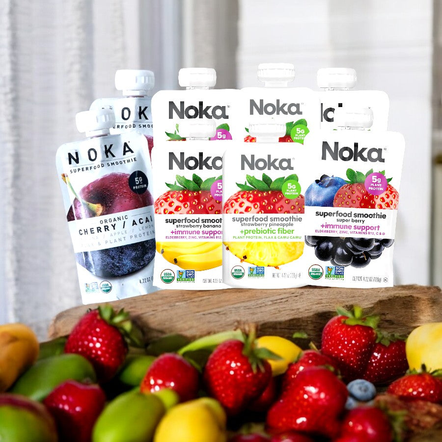 Noka Variety Pack superfood smoothies, featuring 4 flavors with 2 of each for a total of 8 packs, displayed on a wooden surface with various fresh fruits in the foreground.