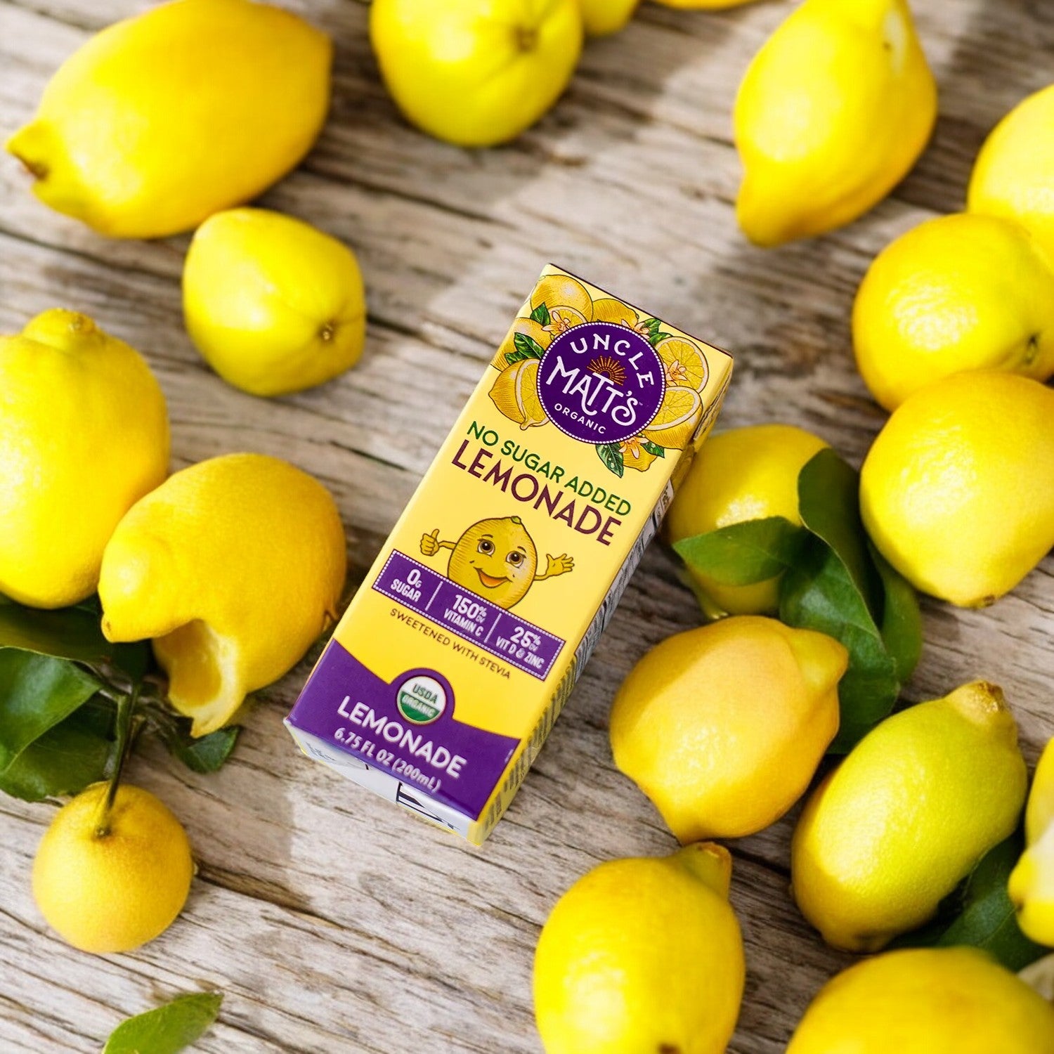 An Uncle Matt's Lemonade Juice Box, 6.75 oz - 1 Count, sits amongst fresh organic lemons on a rustic wooden surface.