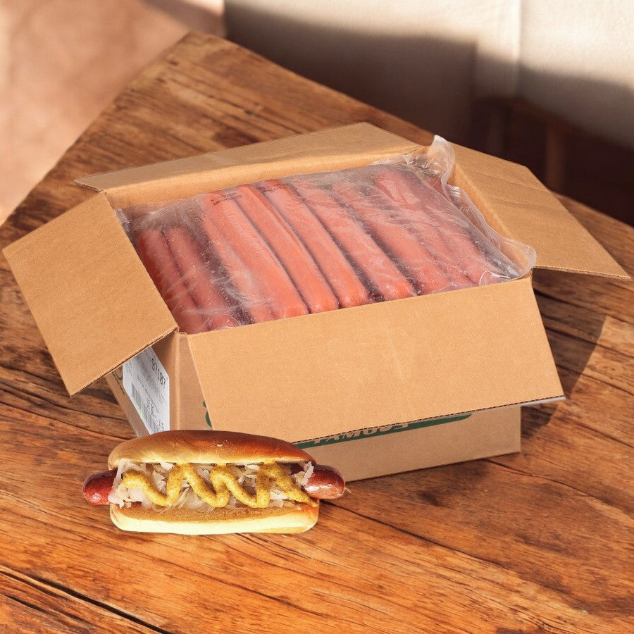 A box of Nathans Famous Frankfurter All-Beef 7" sits open on a wooden table, with one premium beef frank in a bun topped with mustard and onions beside it.