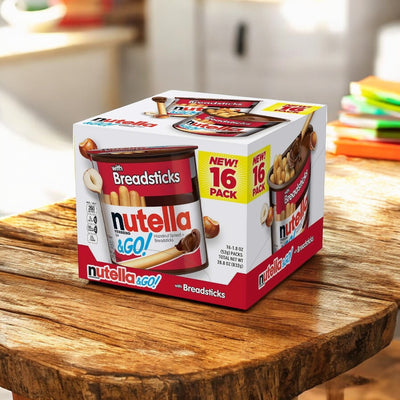 A box of Nutella and Go Hazelnut Spread with Breadsticks Ferrero 16 Pack - 1.8 oz Each, branded "Easy Lunches," featuring a "NEW! 16 PACK" label, sits on a wooden surface with colorful objects blurred in the background.