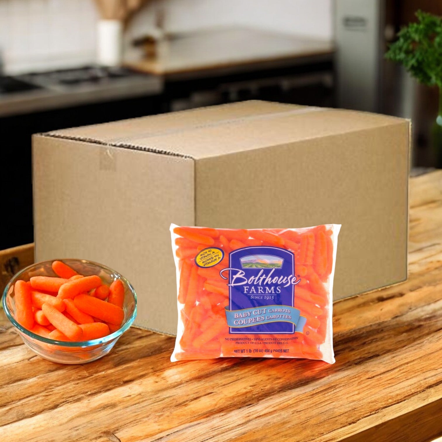 A Bolthouse Farms Carrots Baby Cut Peeled 1.6 oz. pack sits next to a clear bowl of carrots and a large cardboard box on the wooden kitchen counter, providing a perfect portion for a healthy snack.