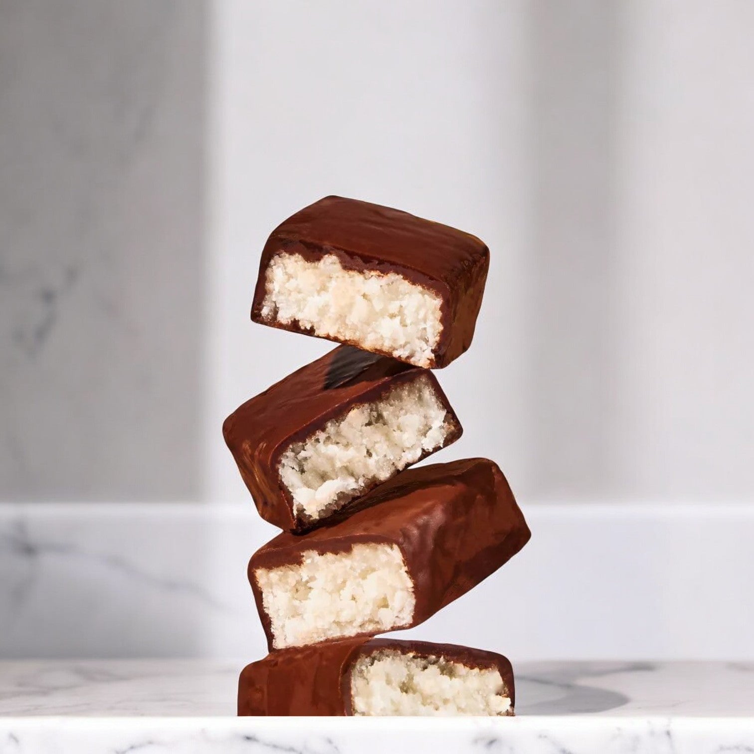 Four Unreal Dark Chocolate Coconut Bars - 1 Count are stacked on top of each other on a white marble surface. These delicious treats from Unreal are Non-GMO, Vegan, and Gluten-Free.