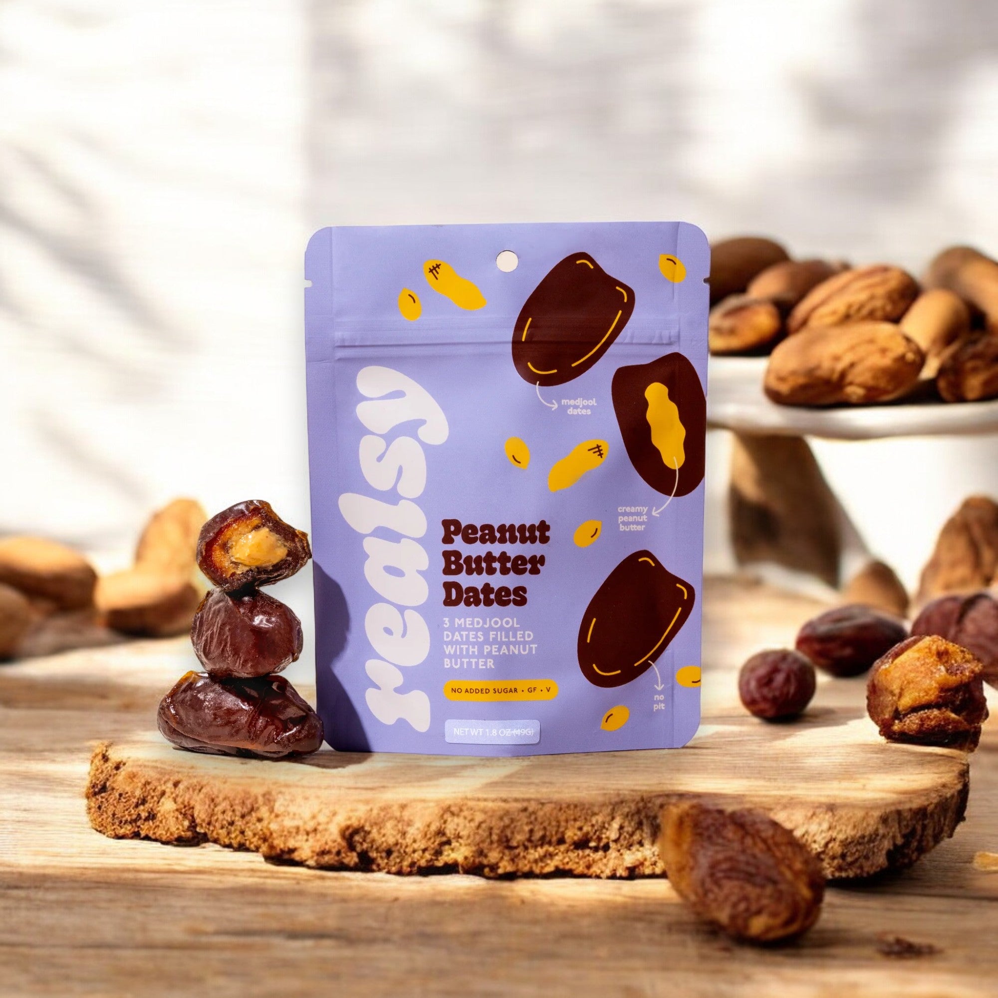 On a wooden surface, a package of "Realsy Peanut Butter Dates" is displayed, surrounded by whole dates and almonds. The packaging clearly states "Medjool Dates Filled with Peanut Butter" along with a "No Added Sugar" label, proudly sourced from our family-owned date farm for lasting energy.