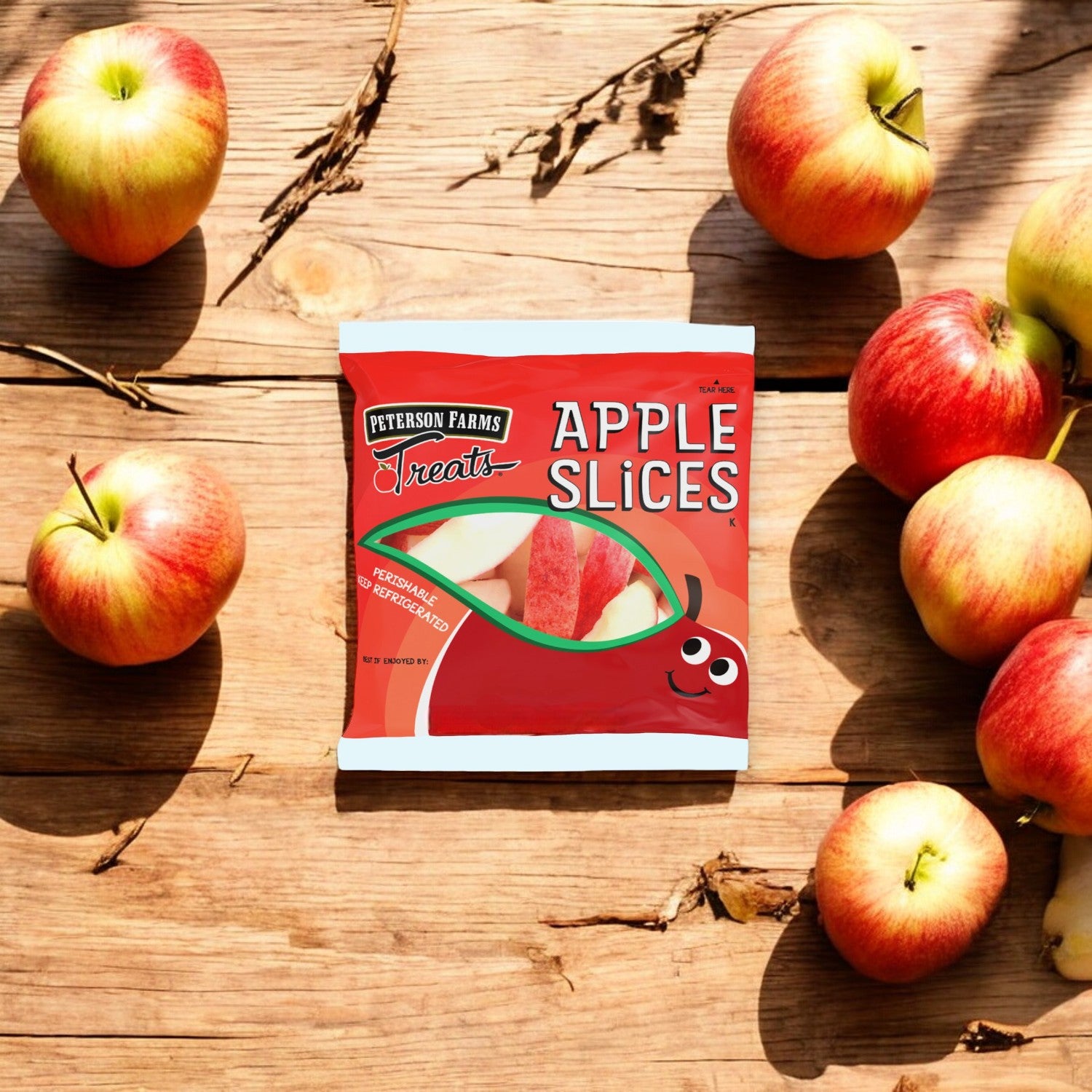 A package of Peterson Farms Fresh Apple Slices, 2 oz. - Bulk 100 Count, is surrounded by whole, fresh apples on a wooden surface, providing a healthy and convenient snacking option.