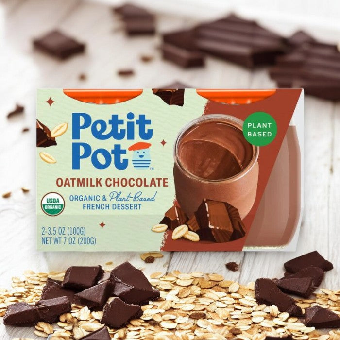 A container from Petit Pot, labeled as Organic Oatmilk Chocolate French Dessert, sits among chocolate pieces and oats. This delectable treat, made with organic oatmilk and entirely plant-based, offers a delightful indulgence for those seeking both taste and health.