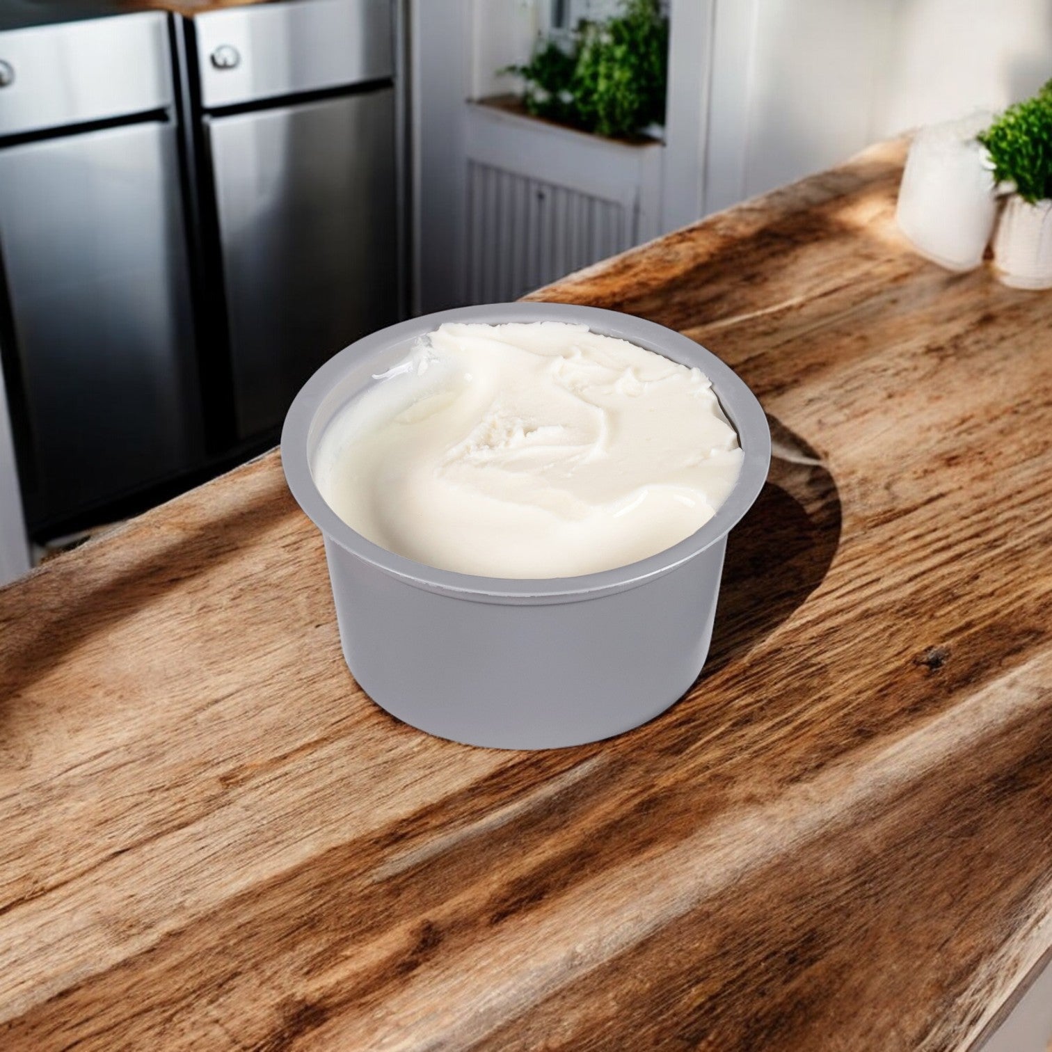 A Kraft Philadelphia Cream Cheese Original Spread Cup sits on a wooden counter with a kitchen background, offering its classic taste.