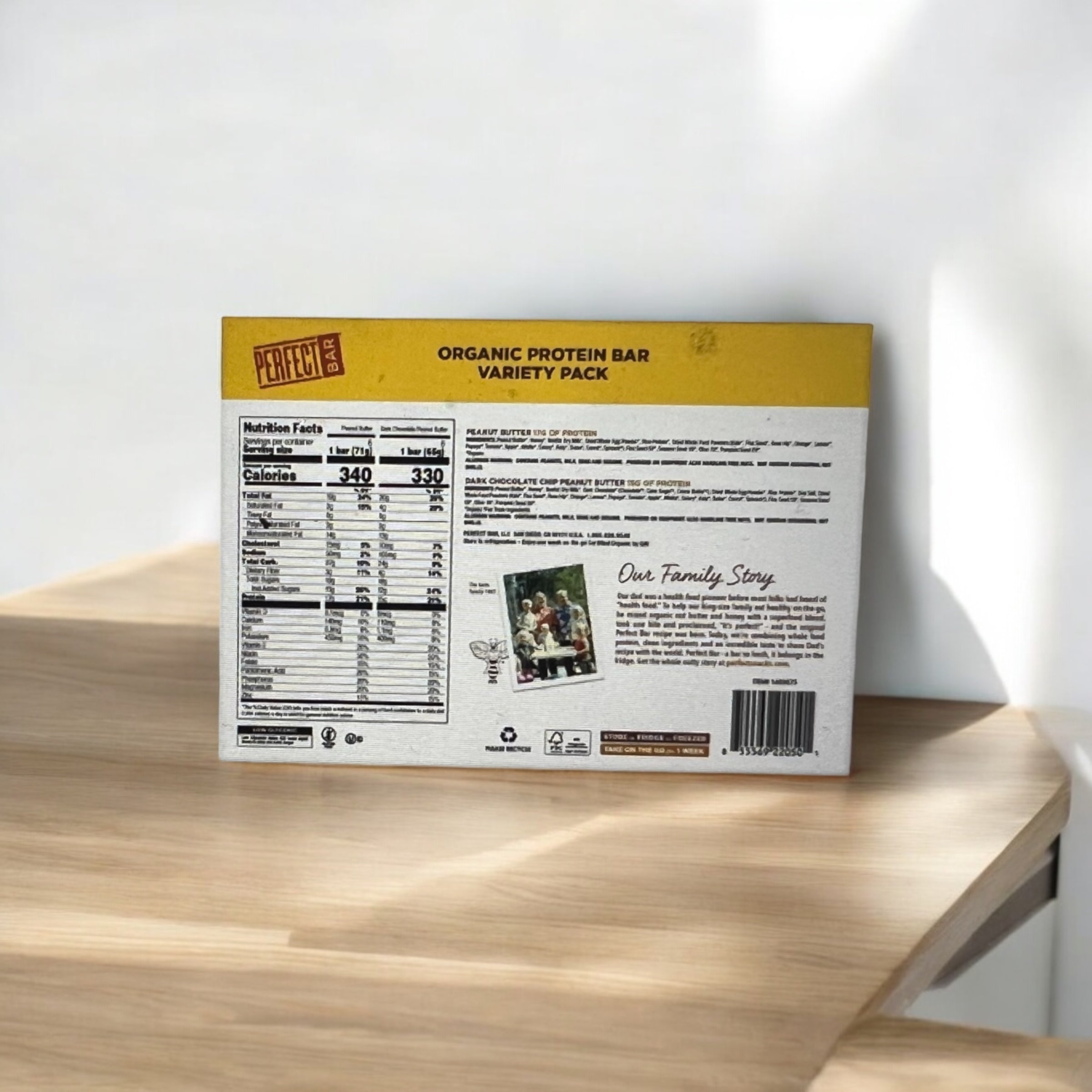 A box of Easy Lunches Perfect Bar Refrigerated Organic Protein Bars (12 count) sits on a wooden surface, showcasing its nutritional information and a section titled "Our Family Story" on the back.