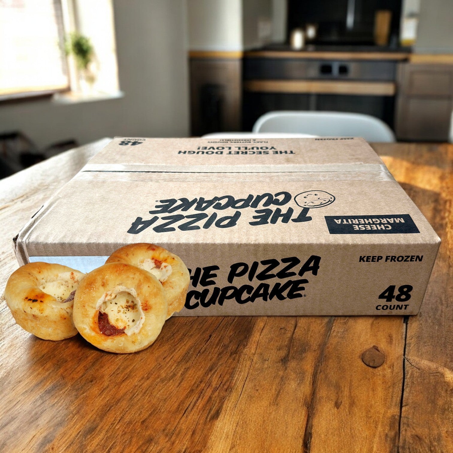 In a cozy kitchen, Pizza Margherita Cupcakes from The Pizza Cupcake brand are enticingly arranged on a wooden table in front of a cardboard box labeled "The Pizza Cupcake," offering an authentic Italian flavor.