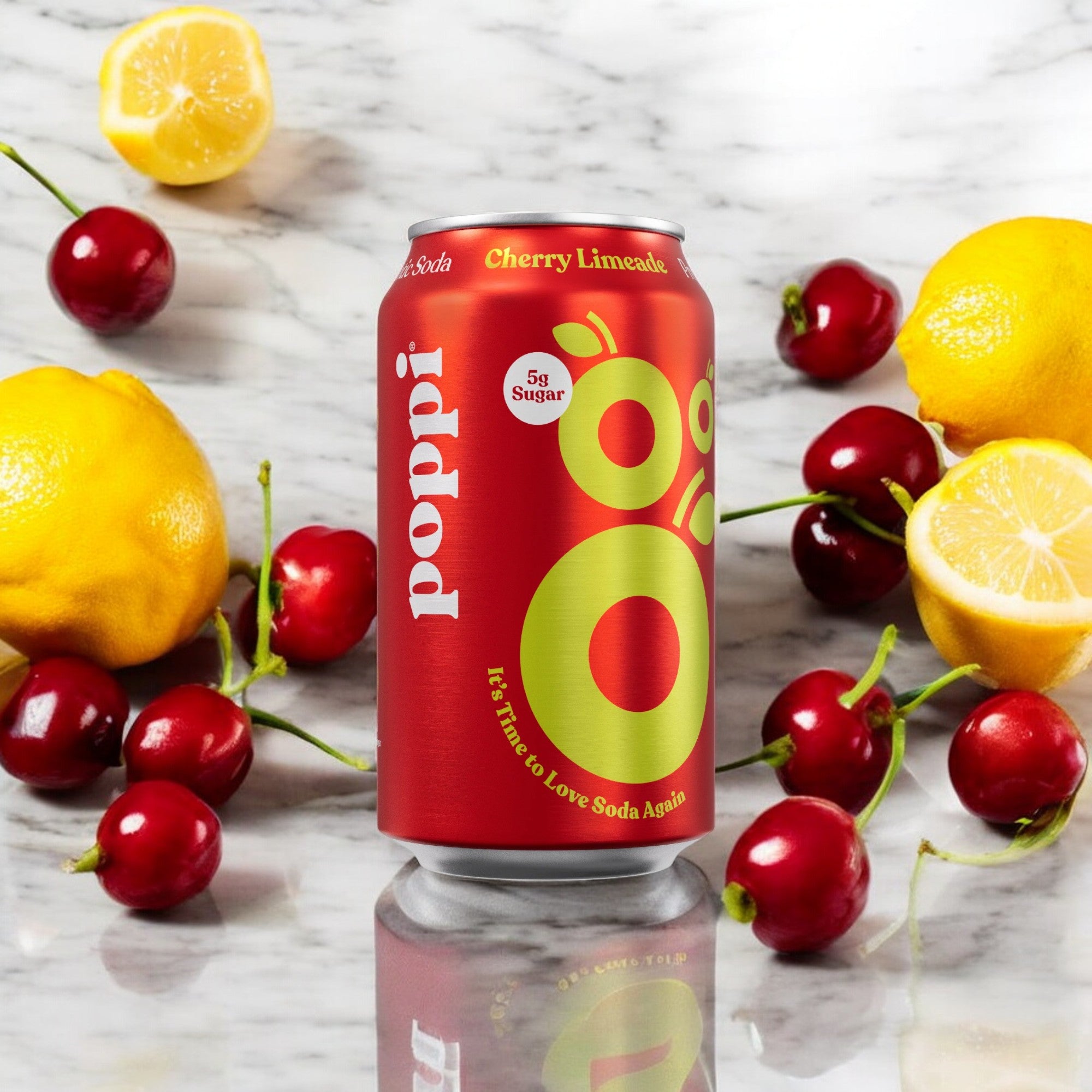 A can of Poppi - Prebiotic Soda Cherry Limeade, 1-12 fl oz Can, is placed on a marble surface, surrounded by fresh cherries and lemons. This refreshing drink from Poppi is delightfully low in sugar.