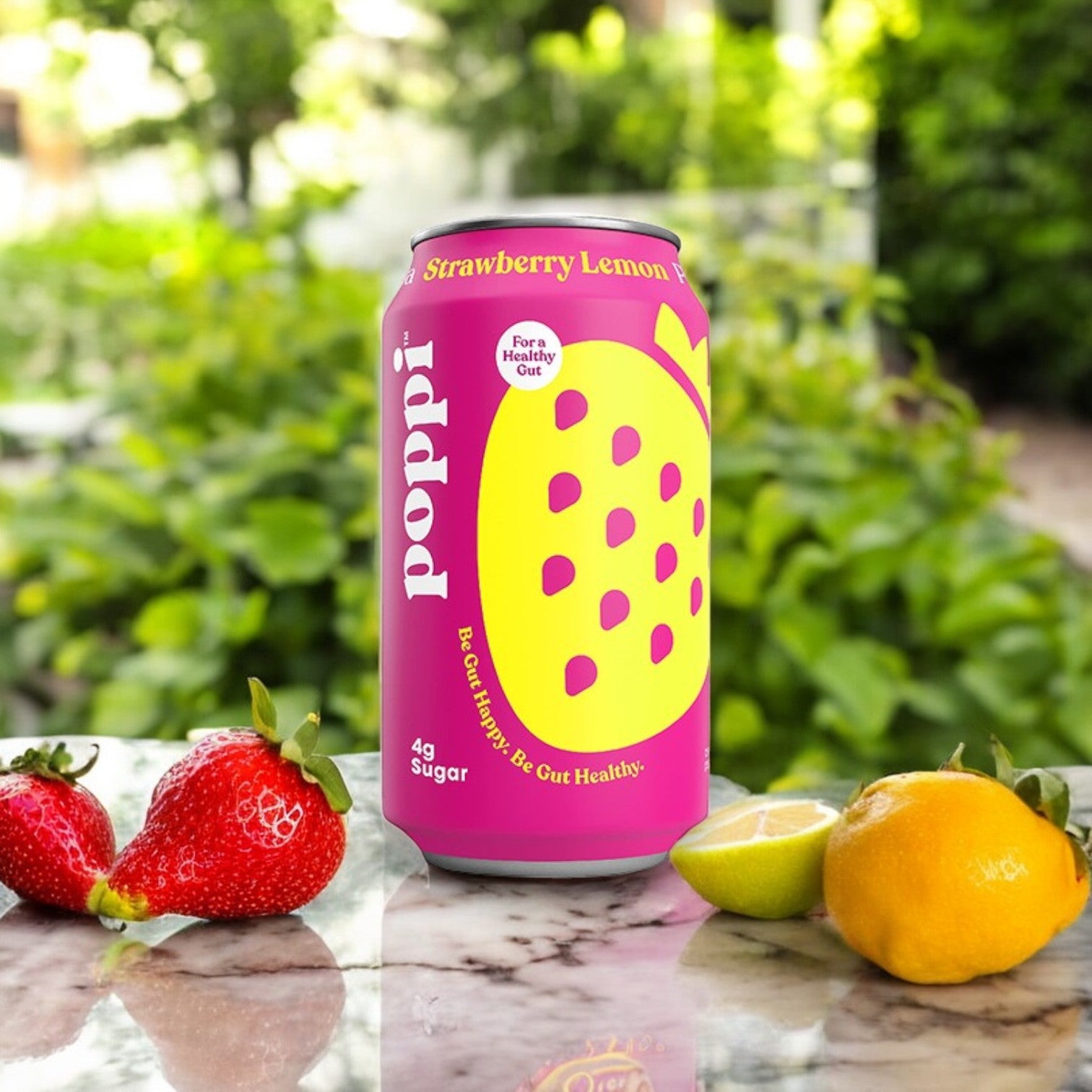 A can of Poppi Prebiotic Soda, Strawberry Lemon, 12 fl oz, from a 4-pack is on a marble surface with strawberries, lemon, and lime in front; greenery decorates the backdrop.