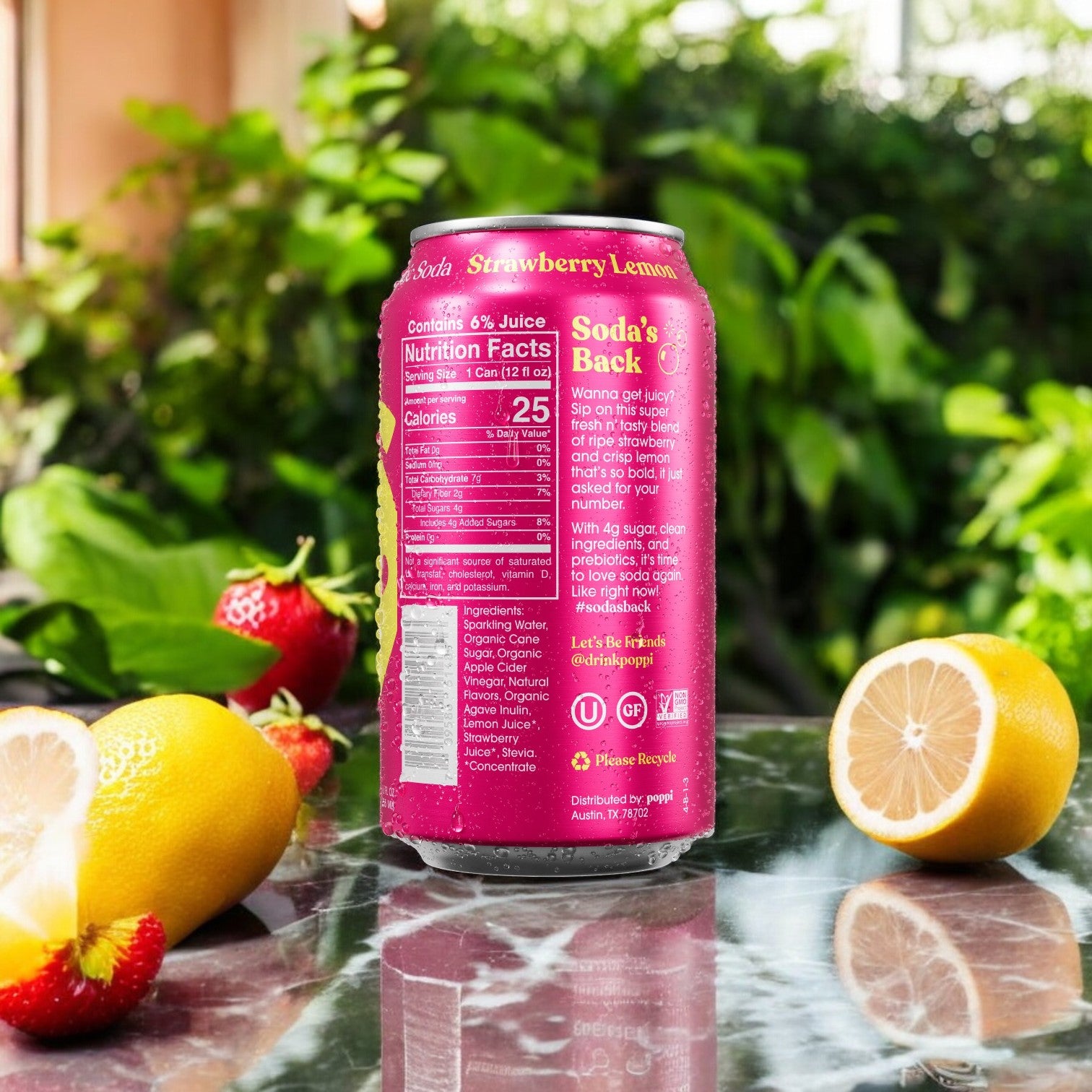 A can of Poppi Prebiotic Soda, Strawberry Lemon flavor, sits on a table with sliced lemon, strawberries, and lime. The low-sugar soda's nutritional facts are visible on the back. Lush greenery adorns the background.