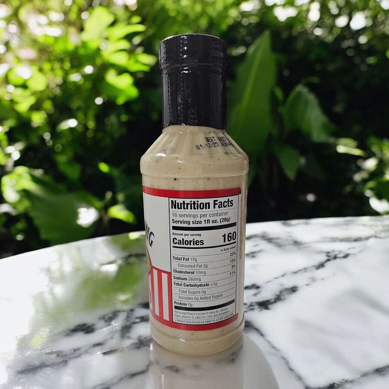 A 16 oz. bottle of Portillo's Caesar Dressing sits on a marble table outside, displaying nutrition facts: 160 calories per serving.