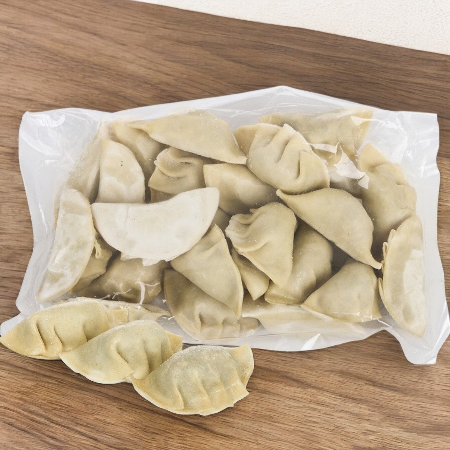 A wooden surface displays a plastic bag containing uncooked Phillip Foods Potsticker Vegetable Shiitake Mushroom dumplings, with a few showcasing their authentic taste placed outside the bag.