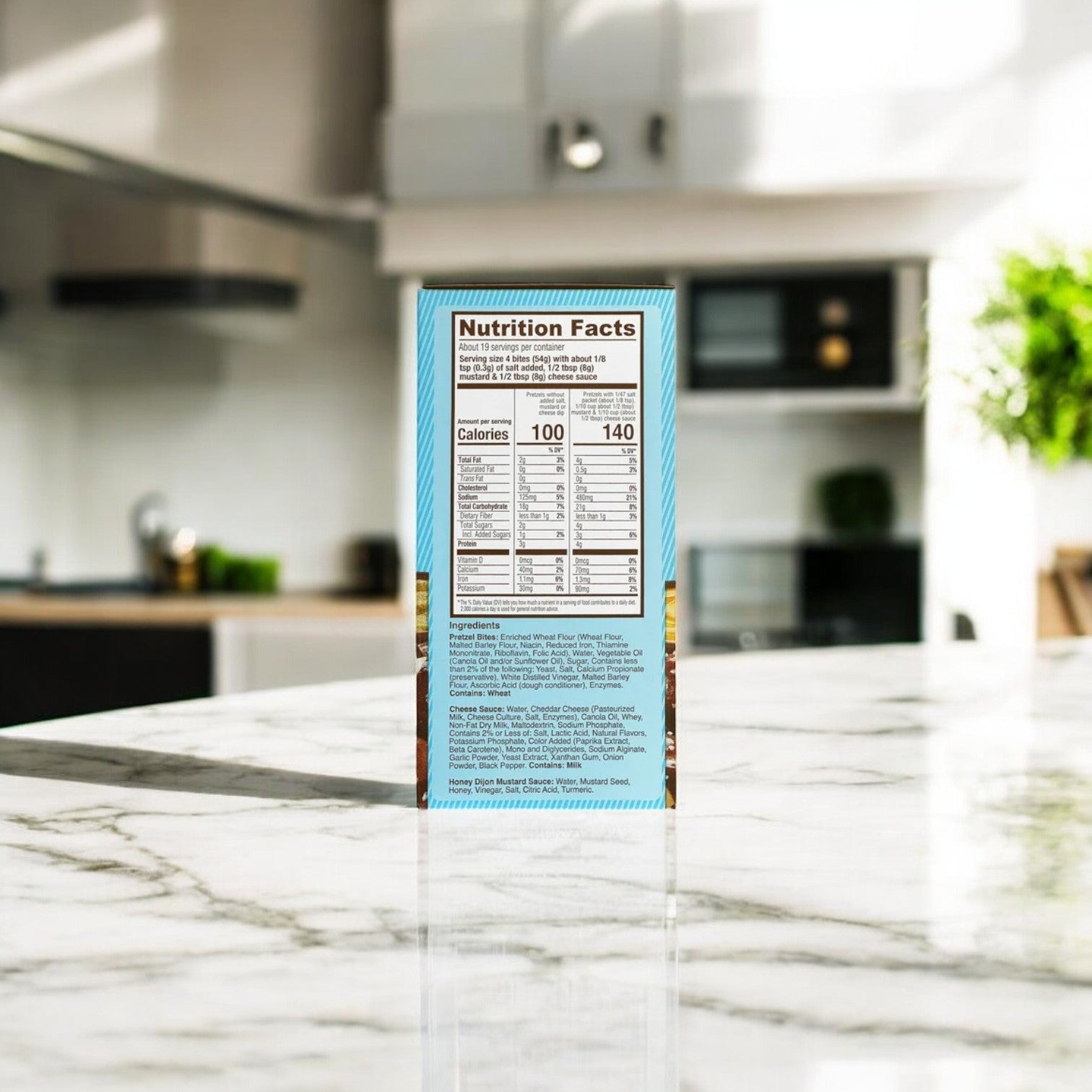 A box of Pretzilla Pretzel Bites, 36.5 oz., is displayed on a marble kitchen countertop next to a resealable bag. The background showcases a modern kitchen with stylish cabinets and lush plants, ideal for satisfying snack cravings.