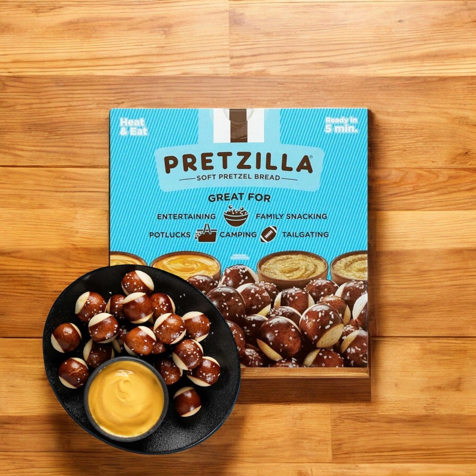 A box of Pretzilla Pretzel Bites (36.5 oz.) sits on a wooden surface, next to a bowl of pretzel bites and cheese dip on a black plate, poised to delight your snack cravings. The resealable bag keeps each bite as fresh and delicious as the first.