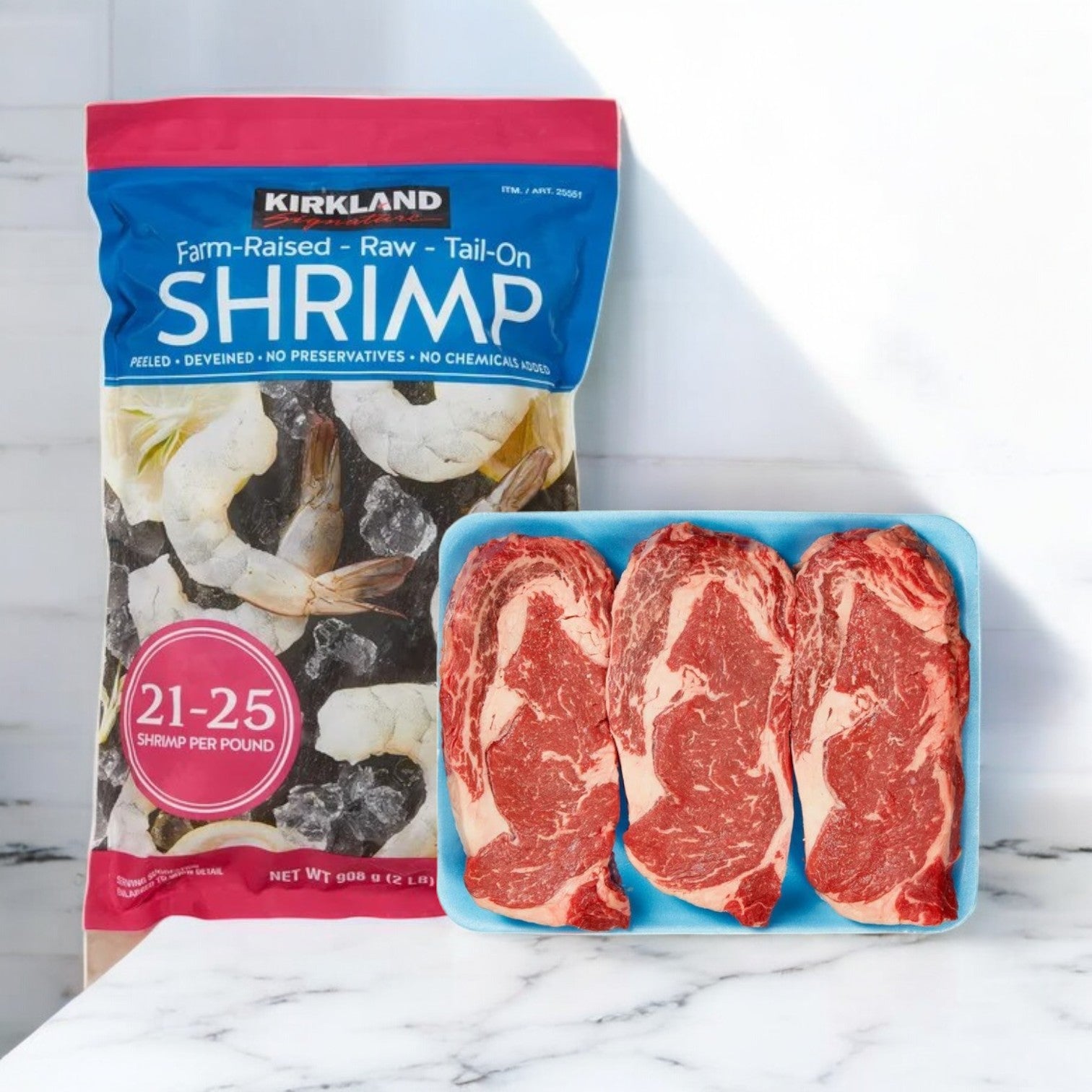 A package from the Easy Lunches Surf & Turf Combo, featuring Kirkland Signature USDA Prime Beef Boneless Ribeye Steak along with farm-raised raw shrimp, rests on a marble surface.