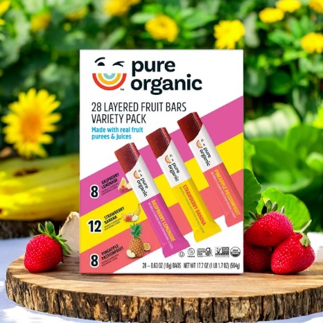 Close-up of a Pure Organic 28 Layered Fruit Bars Variety Pack - 0.63oz - 28 Bars box placed outdoors amidst greenery and strawberries. This wholesome snack variety pack from Pure Organic features layered organic fruit bars in raspberry lemonade, pineapple passionfruit, and strawberry banana flavors.