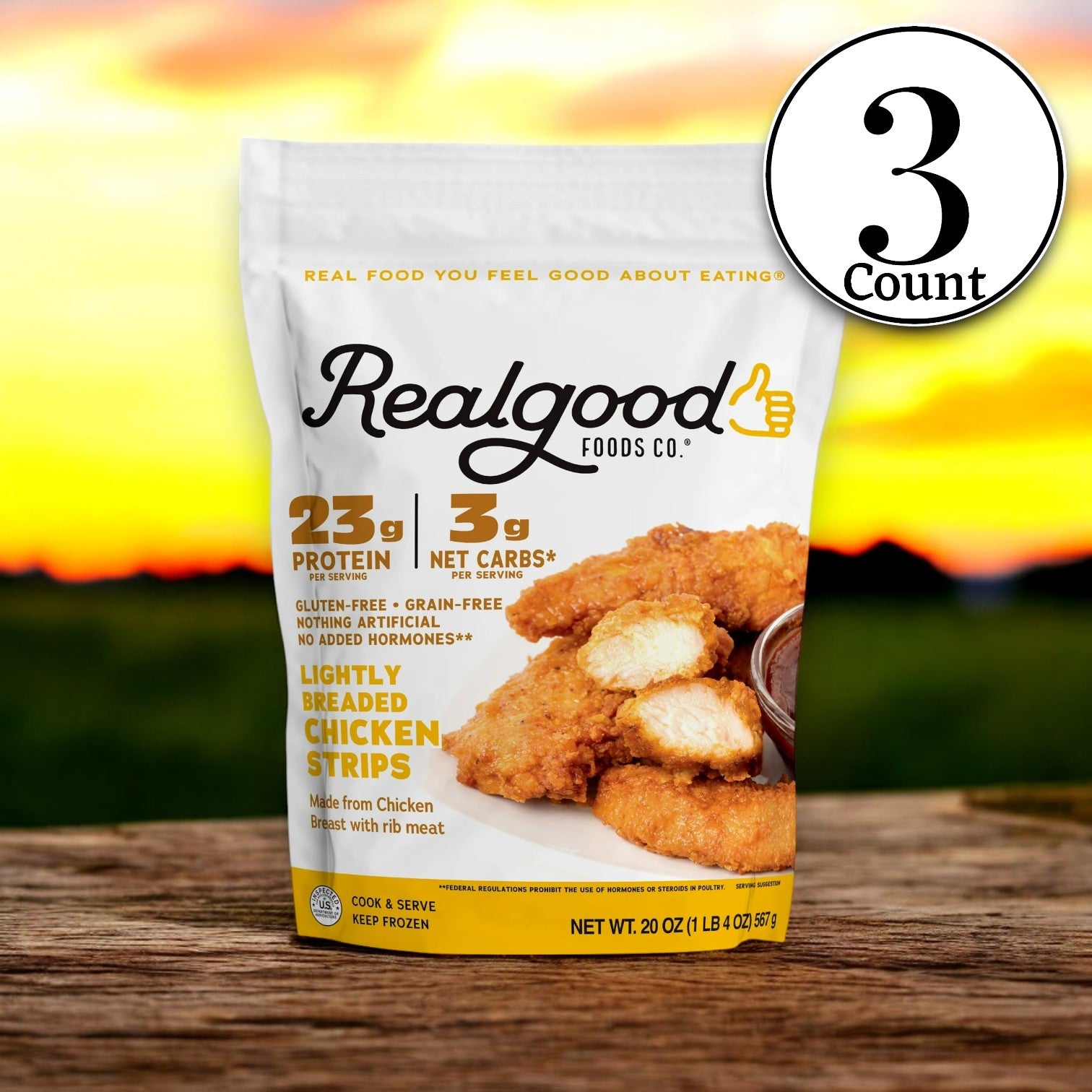 A 20 oz package of Realgood Foods Co. Lightly Breaded Chicken Breast Strips features a set of three labels with nutritional information, all set against a sunset background.