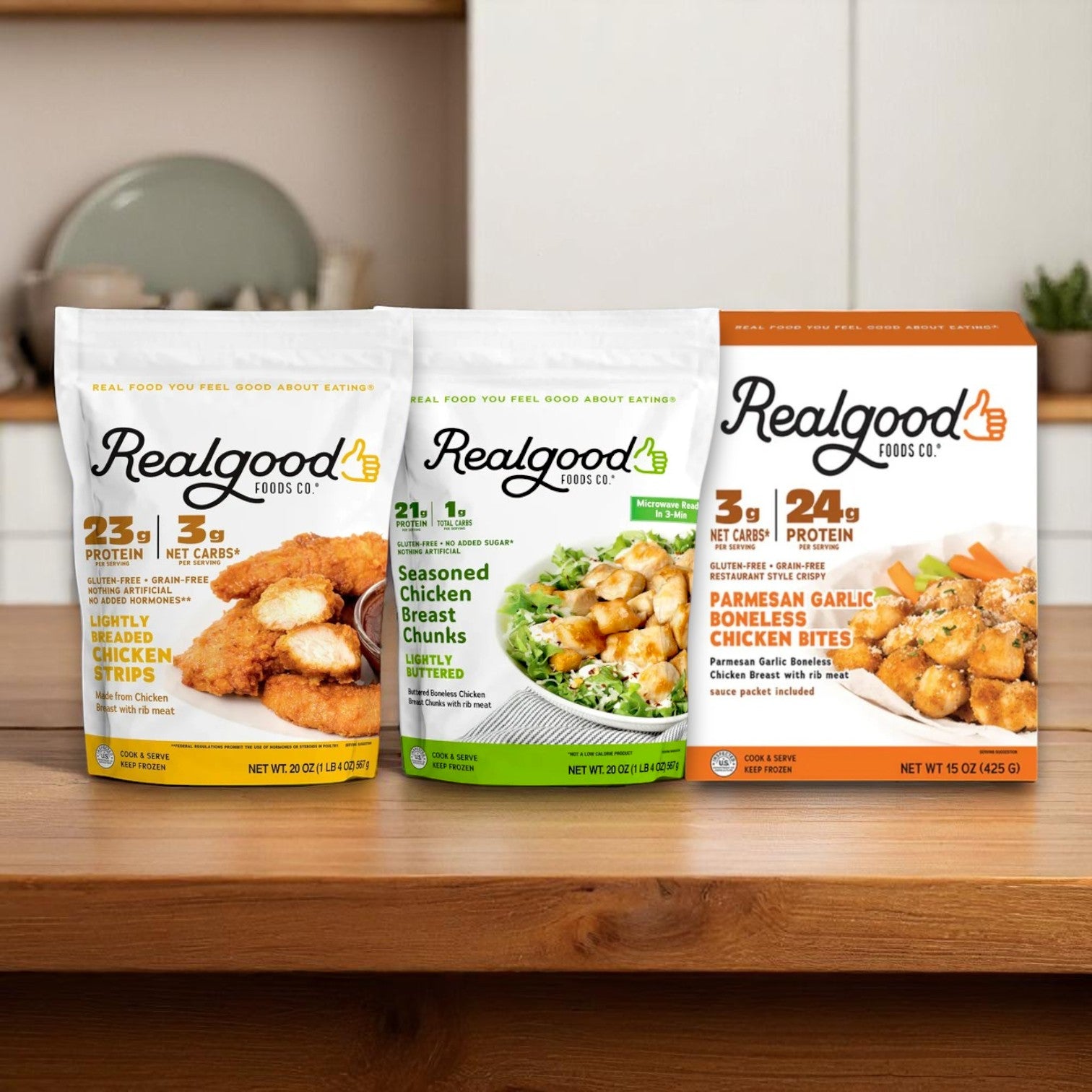 Three packages of Real Good Foods 3-Pack Bundle – Low Carb, High Protein Chicken Favorites (Gluten-Free) are shown on a wooden kitchen surface.