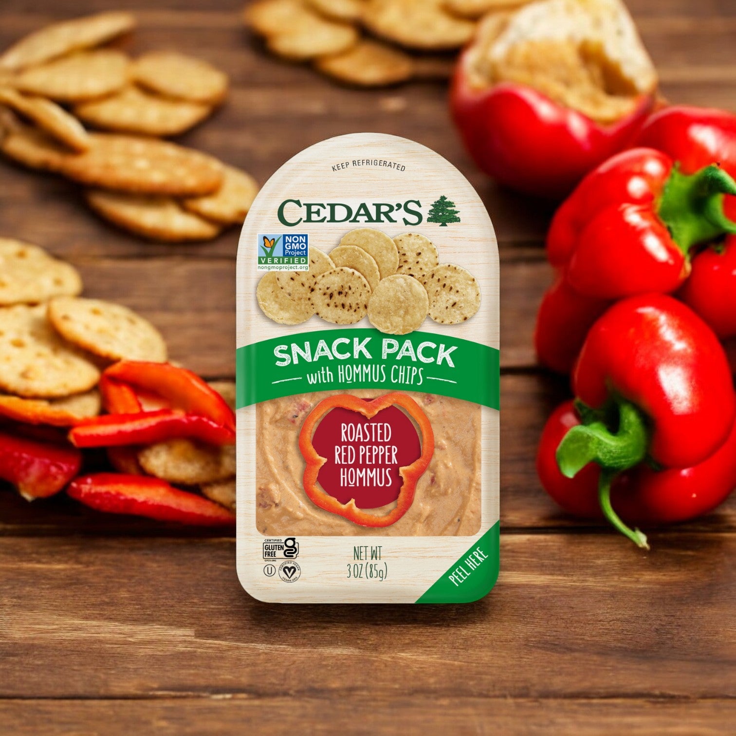 Cedar's Roasted Red Peppers Hommus with Hommus Chips -1 Count, from the Cedar's brand, offers a delightful snack option with roasted red pepper hummus and crispy chips, beautifully complemented by sliced red bell peppers and chips on a wooden surface.