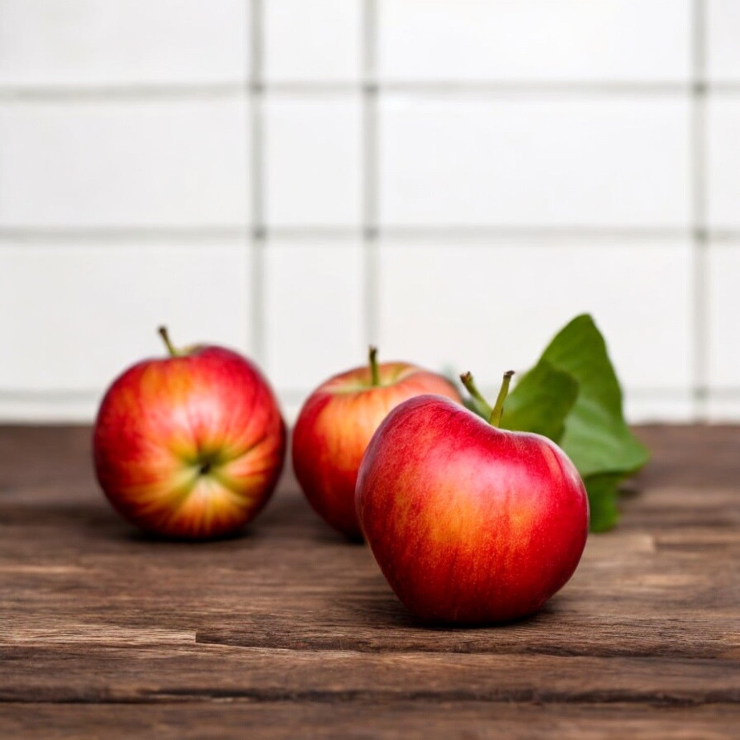 Three pounds of Easy Lunches Honeycrisp Apples, adorned with green leaves, rest on a wooden surface against a backdrop of white tiled wall, showcasing their juicy crunch texture.