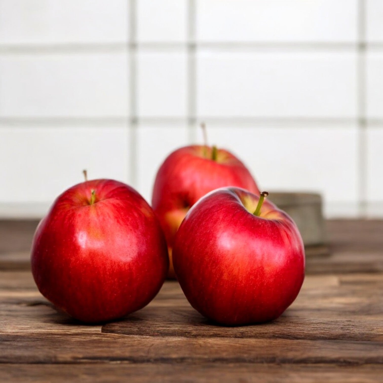 Three Organic Apples from Easy Lunches are placed on a wooden surface with a tiled wall in the background.